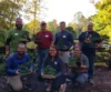 Smiling group holding bonsai trees outdoors