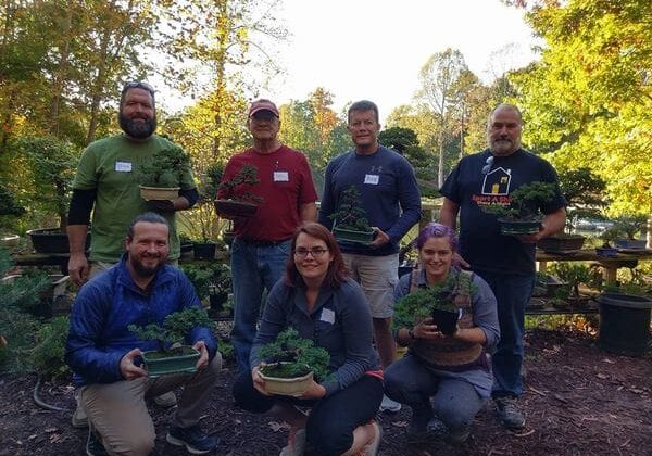 Bonsai workshop group holding potted trees outdoors